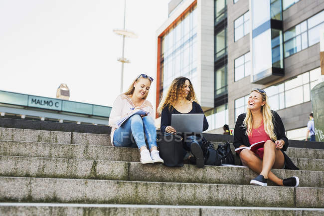 Three young women with laptop, sitting on steps — Stock Photo