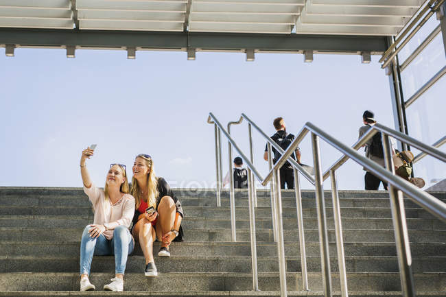 Mujeres sentadas en escalones, tomando selfie - foto de stock