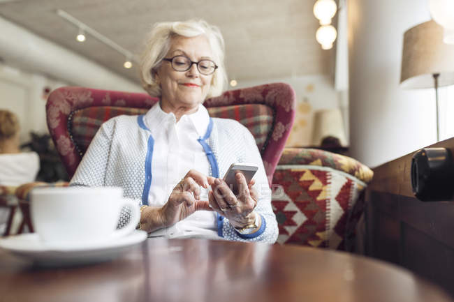 Seniorin benutzt Handy während Kaffeepause in Café — Stockfoto