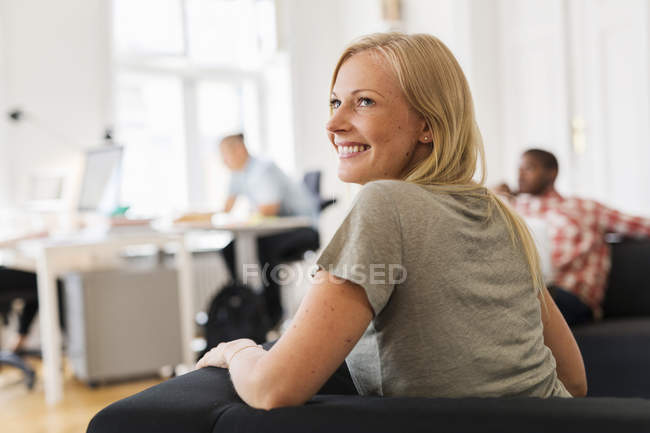Усміхнена жінка сидить на дивані в офісі — стокове фото