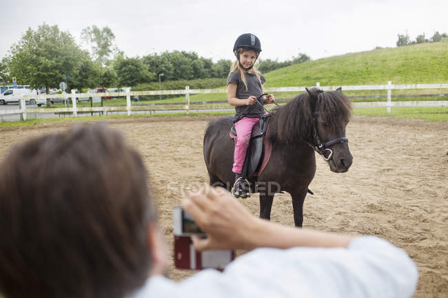 Person photographing girl (4-5) on pony — Stock Photo