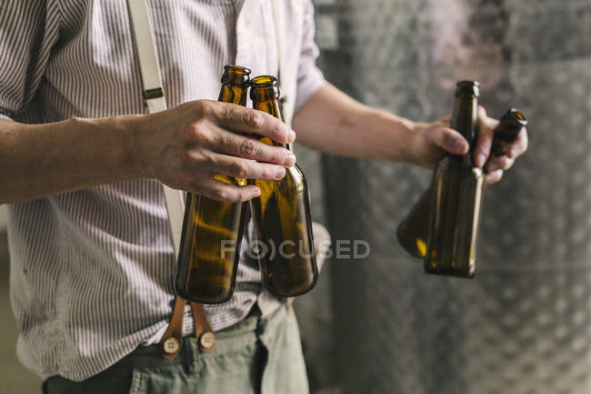 Sección media del trabajador cervecero sosteniendo botellas de cerveza vacías - foto de stock