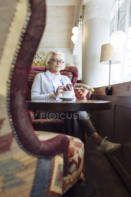 Mujer mayor usando el teléfono móvil durante la pausa para el café en la cafetería - foto de stock