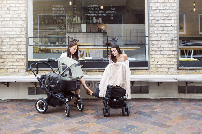 Две молодые матери с детскими колясками сидят перед кафе — стоковое фото