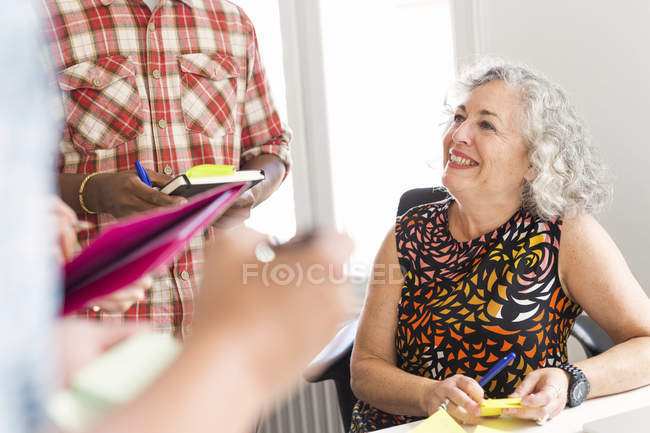 Улыбающаяся женщина, ведущая деловую встречу, коллеги, пишущие в блокноте — стоковое фото