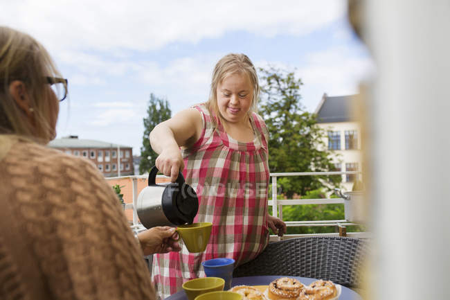 Tochter mit Down-Syndrom gießt Kaffee für Mutter auf Balkon — Stockfoto