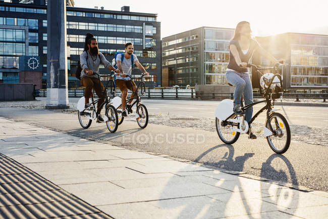 Tres personas en bicicleta en la ciudad - foto de stock