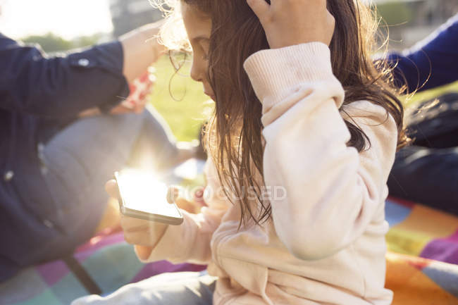 Parents avec leur fille (4-5) au pique-nique en ville, fille utilisant un téléphone intelligent — Photo de stock