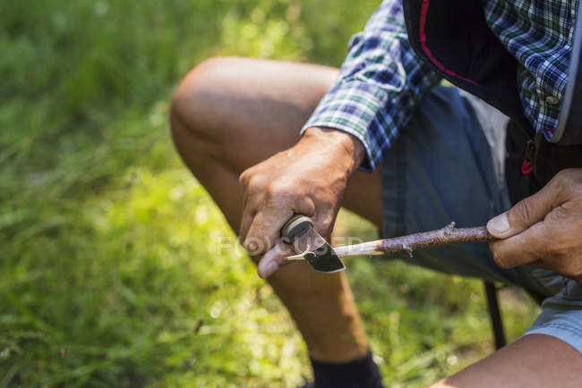 Man sharpening stick  at forest during daytime — Stock Photo