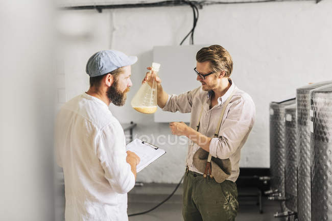Brewery workers examining beer in beaker — Stock Photo