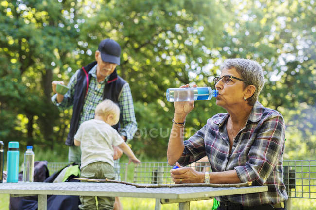 Женщина пьет воду за столом для пикника — стоковое фото