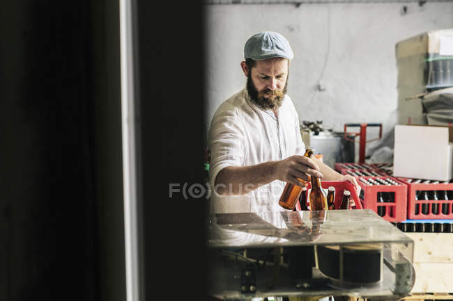 Trabalhador da cervejaria colocando garrafas de cerveja na caixa — Fotografia de Stock