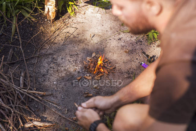 Hombre encendiendo fuego de campamento en el bosque - foto de stock