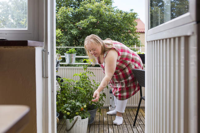 Mulher com síndrome de down olhando para as plantas na varanda — Fotografia de Stock