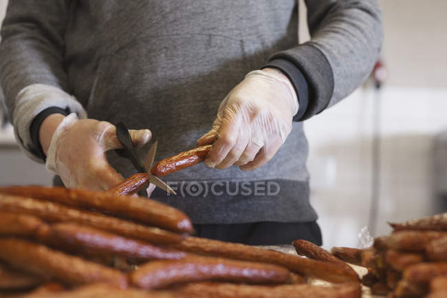 Sección media del hombre cortando salchichas con tijeras - foto de stock