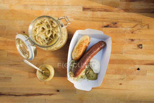 Studio shot of pork sausage with bread roll and mustard in paper bag — Stock Photo
