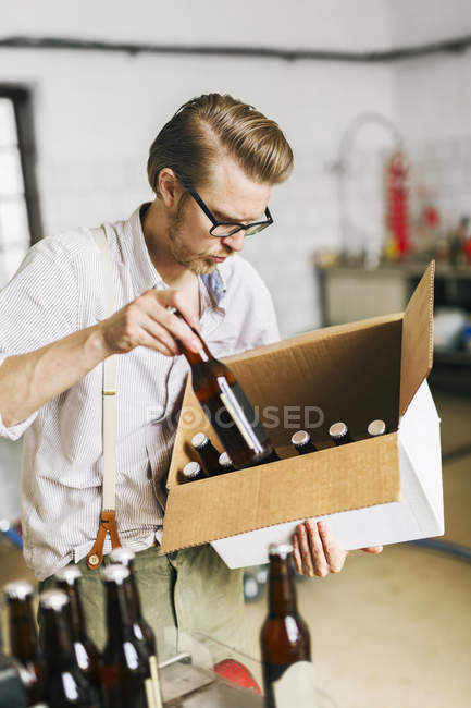 Працівник пивоваріння вставляє пляшки пива в картонну коробку — стокове фото