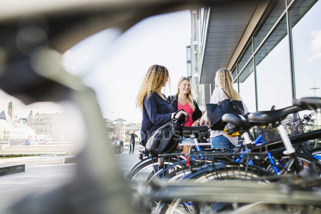 Three young women standing by bicycles — Stock Photo