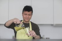 Hombre verter smoothie en vidrio en la cocina - foto de stock