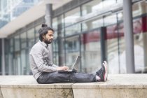 Empresário sentado no parapeito e trabalhando no laptop — Fotografia de Stock