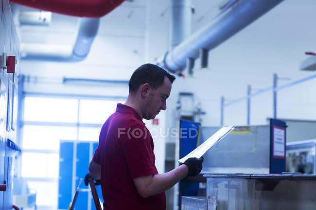 Hombre leyendo papeles en planta industrial - foto de stock
