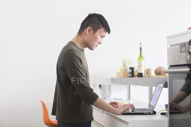 Чоловік працює на ноутбуці на кухонній стійці — стокове фото