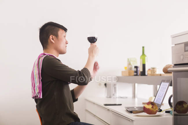 Hombre de pie con copa de vino en la cocina - foto de stock