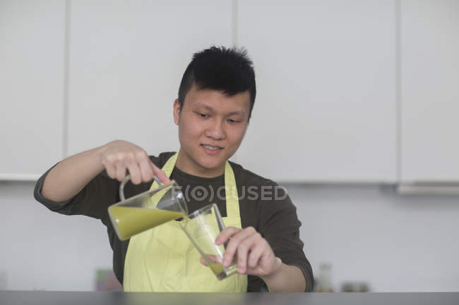 Мужчина наливает смузи в стекло на кухне — стоковое фото