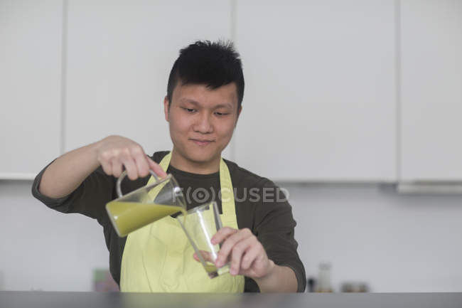Uomo versando frullato in vetro in cucina — Foto stock