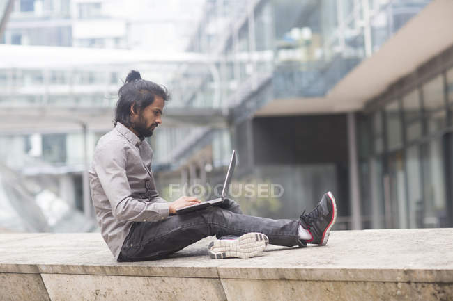 Homme d'affaires assis sur parapet et travaillant sur ordinateur portable — Photo de stock