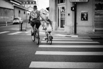 Homem cruzando estrada com filha em bicicletas — Fotografia de Stock