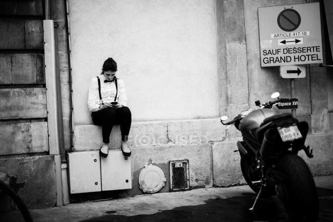 Офіціант дівчина сидить на парапету і за допомогою смартфона — стокове фото