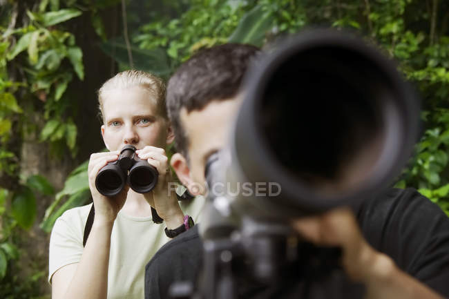 Mujer bonita con prismáticos y hombre con telescopio en la selva - foto de stock