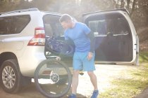 Чоловік бере гірський велосипед з багажника автомобіля — стокове фото
