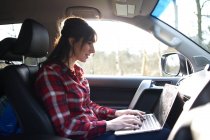 Femme assise dans la voiture et utilisant un ordinateur portable — Photo de stock
