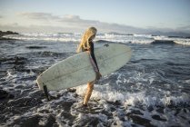 Frau mit Surfbrett in der Hand läuft über Felsen — Stockfoto