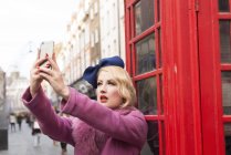 Woman taking selfie outside telephone kiosk — Stock Photo