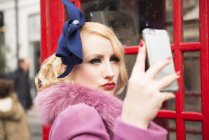 Женщина делает селфи возле телефонного киоска — стоковое фото