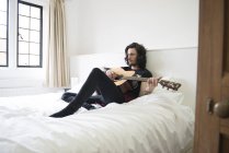 Uomo sdraiato sul letto e suonare la chitarra — Foto stock