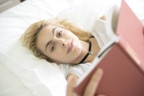 Woman lying on bed reading — Stock Photo