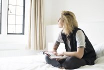 Frau mit Tätowierungen sitzt auf Bett und liest — Stockfoto
