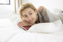 Mulher com tatuagens deitada na cama com livro — Fotografia de Stock