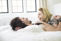 Пара лежить на ліжку і сміється разом — стокове фото