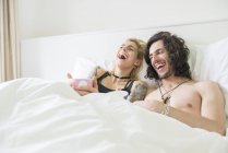 Пара лежить в ліжку насолоджуючись чаєм і сміючись — стокове фото