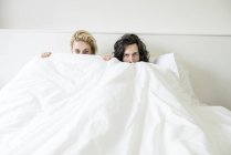 Пара в постели, играющая в прятки с камерой — стоковое фото