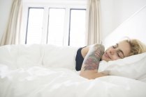 Tattooed woman asleep in bed — Stock Photo