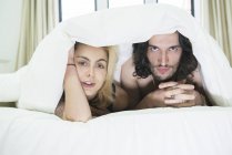 Paar guckt unter Bettdecke hervor — Stockfoto