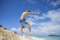 Garçon sautant dans les dunes de sable à la plage — Photo de stock