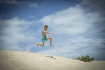 Menino pulando em dunas de areia na praia — Fotografia de Stock