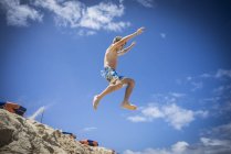 Niño saltando en dunas de arena en la playa - foto de stock